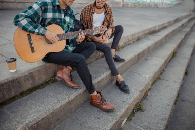 Gitarla merdivenlerde oturan iki erkek arkadaş gülümsüyor.