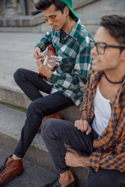 İki kardeş basamaklarda gitarla oturuyor.