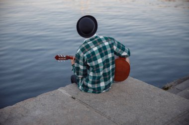Genç erkek gitarla dışarıda oturuyor.