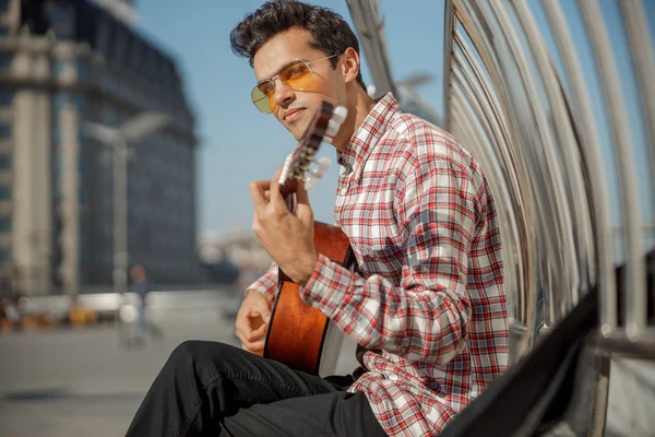Mladý muž sedí ve městě a drží kytaru — Stock fotografie
