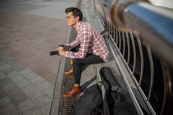 Ung gitarrist med varm dryck vilar utomhus — Stockfoto