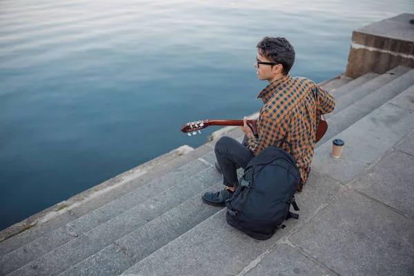 Junger Mann sitzt auf Stufen, während er Gitarre spielt — Stockfoto