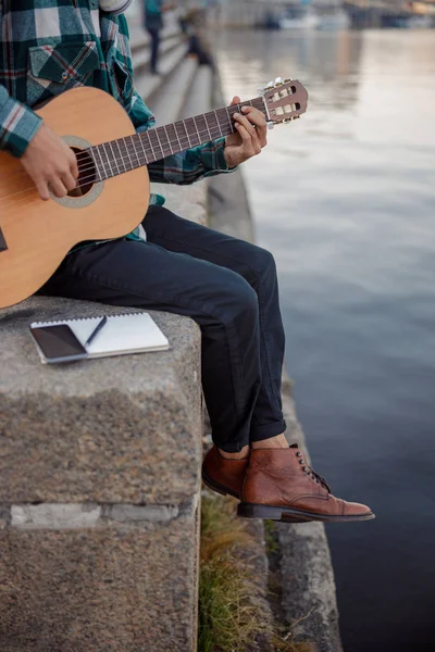 Гитарист сидит с ноутбуком и смартфоном на улице — стоковое фото