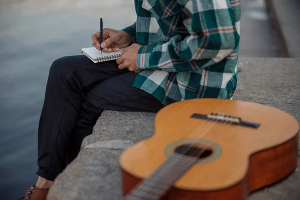 Jovem com guitarra sentado perto do rio — Fotografia de Stock