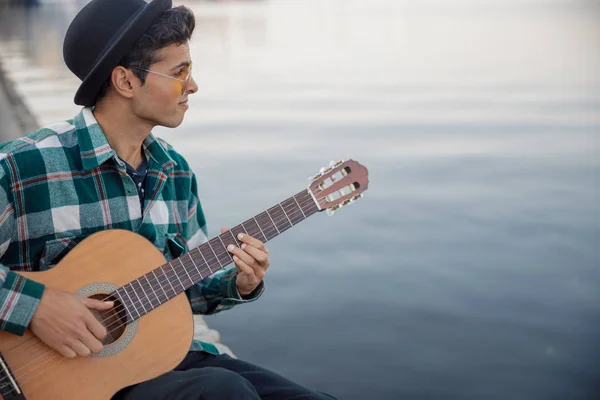 Sorrindo cara com guitarra sentado perto do rio — Fotografia de Stock