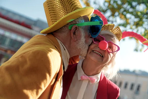 Hombre de edad en traje de payaso besar esposa al aire libre stock foto — Foto de Stock