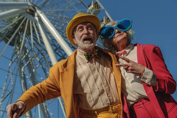 Radostný starý pár ve směšném oblečení v blízkosti atrakce — Stock fotografie