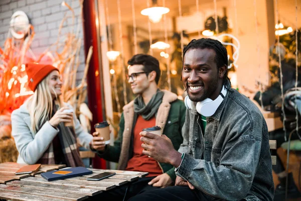 Улыбающийся афроамериканец смотрит в камеру, сидя в кафе — стоковое фото