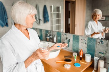 Elinde haplar ve bir bardak su tutan gülümseyen yaşlı kadın.