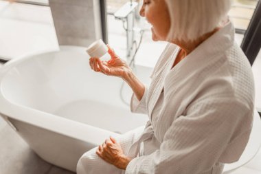 Gülümseyen yaşlı bayan elinde krema kavanozu tutuyor.