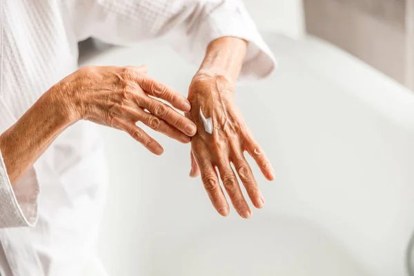Mulher velha aplicando creme cosmético na mão — Fotografia de Stock