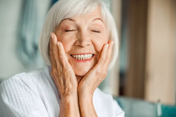 Cheerful elderly lady touching her face and closing eyes — Stock Photo, Image