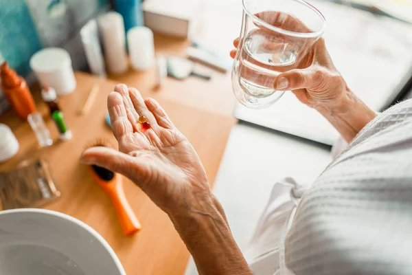 Elderly woman holding pills and glass of water — Stock Photo, Image