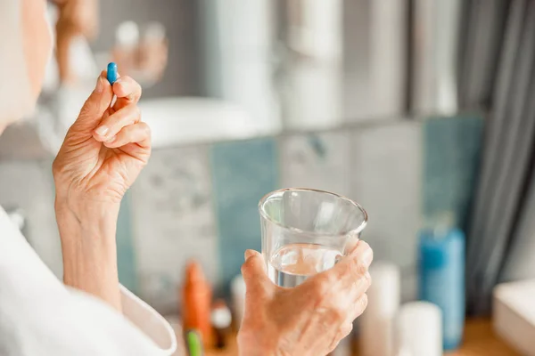 青い錠剤と水のガラスを保持する高齢女性 — ストック写真