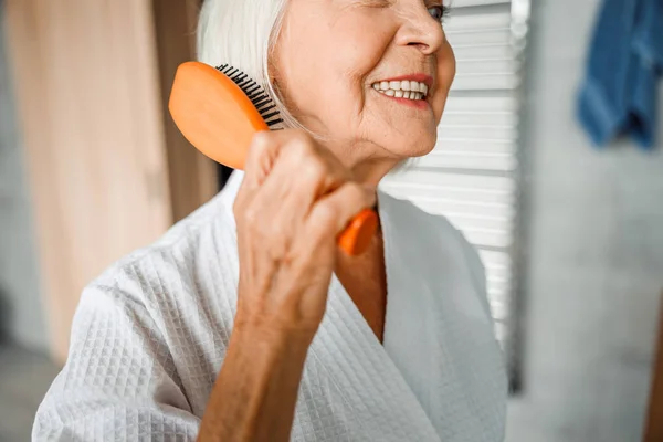Fröhliche ältere Frau, die sich die Haare putzt und lächelt — Stockfoto