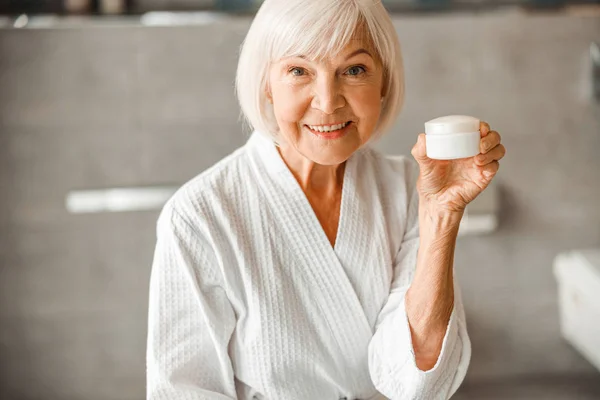 Cheerful old lady holding jar of cream — Stock Photo, Image