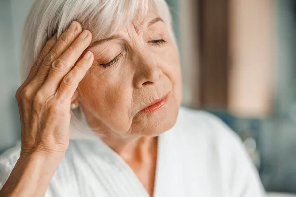 Mutsuz yaşlı kadın alnına dokunuyor ve başı ağrıyor. — Stok fotoğraf
