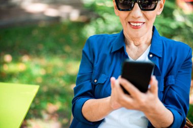 Sokakta akıllı telefon kullanan neşeli, olgun bir bayan.