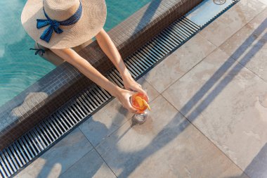 Yazlık şapkalı genç kadın elinde bir bardak kokteyl tutuyor.