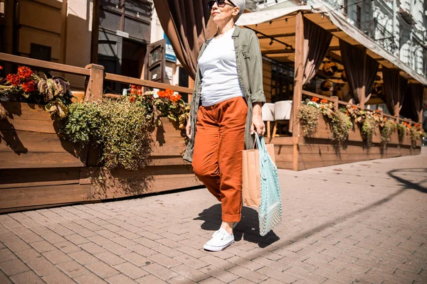 Sorridente signora anziana passeggiando lungo la strada della città — Foto Stock