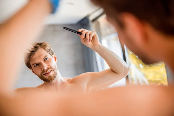 Улыбающийся молодой человек расчесывает волосы в ванной — стоковое фото