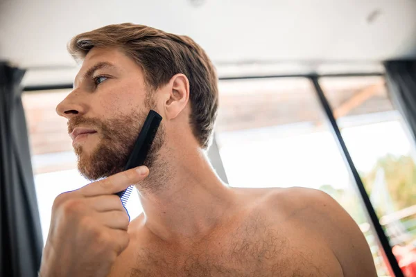 Bonito jovem escovando sua barba no banheiro — Fotografia de Stock