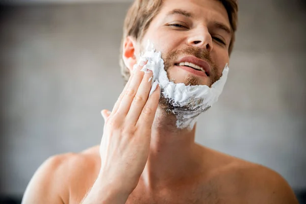 Joven alegre aplicando crema de afeitar en la cara —  Fotos de Stock