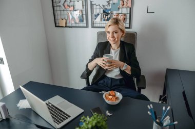 Güzel genç bayan iş yerinde sıcak içecekle dinleniyor.