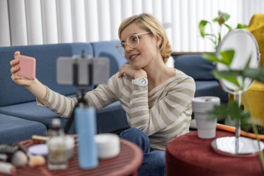 Gülümseyen kadın blogcu akıllı telefon kullanırken kameraya poz veriyor