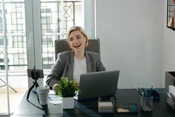 Усміхнена красива жінка сидить у своєму офісі — стокове фото