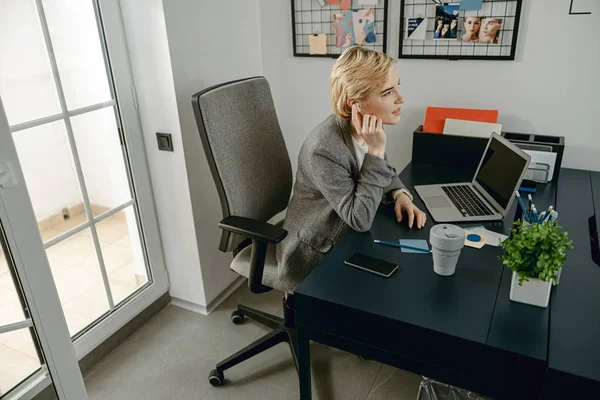 Jovem mulher tocando fone de ouvido em seu local de trabalho — Fotografia de Stock
