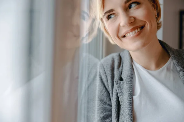 Smiling attractive woman is standing near window — Stock Photo, Image