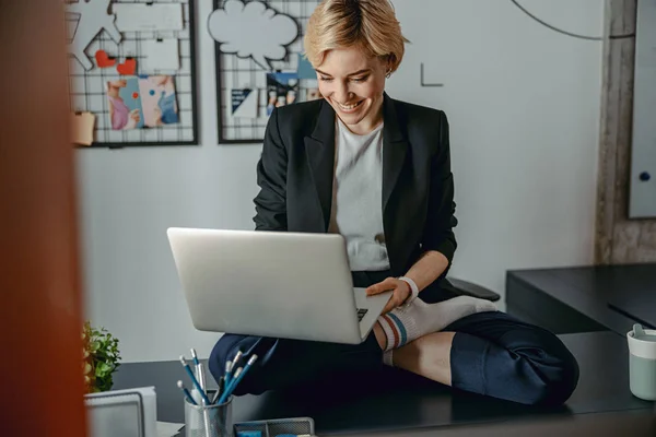 Glückliche hübsche Frau sitzt auf dem Desktop mit Laptop — Stockfoto