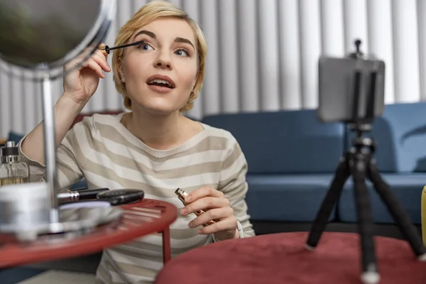 Beautiful young female showing makeup on camera in living room — Stock Photo, Image