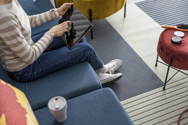 Молодая женщина сидит на диване с гаджетом
