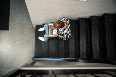 Genç adam dizüstü bilgisayarla merdivenlerde yazı yazıyor.