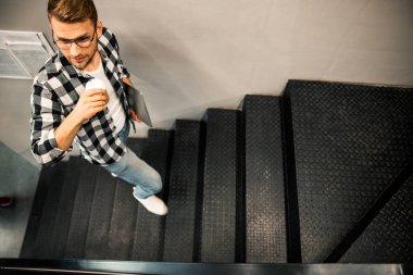 Genç adam sıcak içeceklerle merdivenlerden çıkıyor.