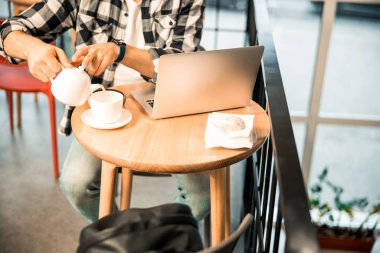 Genç adam kafede fincana çay dolduruyor.