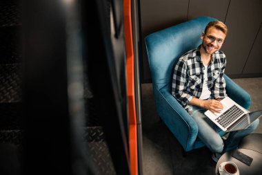 Gülümseyen genç adam dizüstü bilgisayar kullanıyor ve kameraya bakıyor.