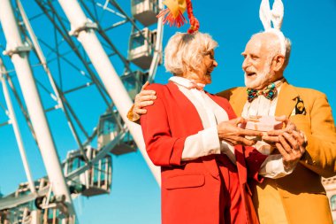 Gülümseyen yaşlı adam dışarıda güzel bayana sarılıyor.