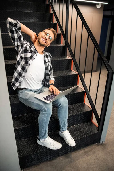 Jeune homme souriant dans des lunettes assis sur les escaliers — Photo