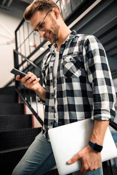 Sorrindo masculino de pé e olhando no smartphone — Fotografia de Stock