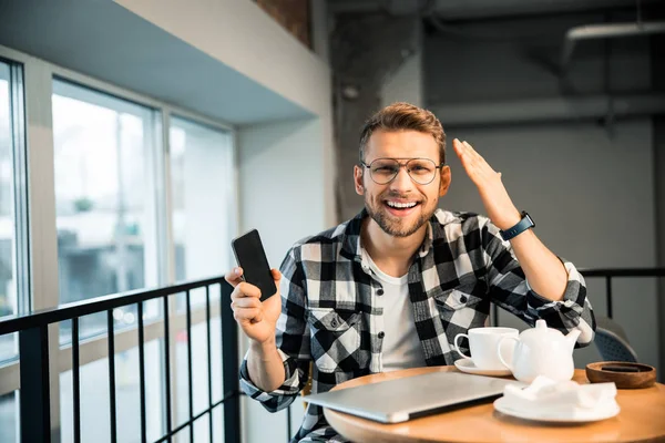 Jovem feliz com telefone celular sentado na casa de café — Fotografia de Stock