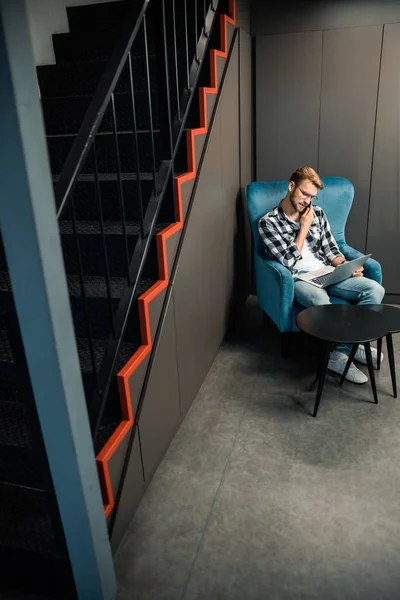 Young male sitting with laptop and holding smartphone — 스톡 사진