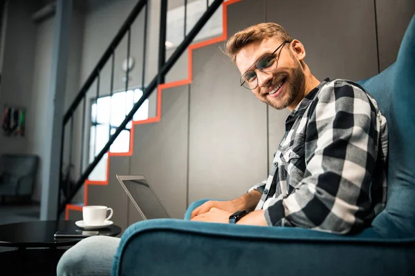 Sorrindo cara jovem trabalhando com laptop dentro de casa — Fotografia de Stock