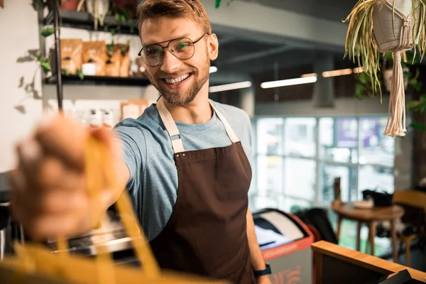 Счастливый молодой человек в фартуке во время работы в кафе — стоковое фото
