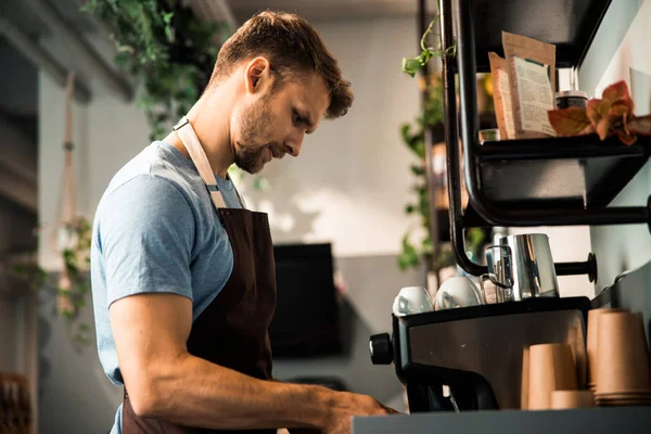 Young man standing near professional coffee machine — 스톡 사진