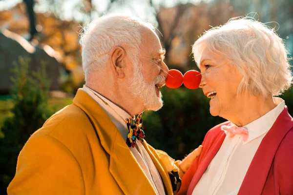 Sonriendo viejo marido y mujer con narices de payaso en el parque — Foto de Stock