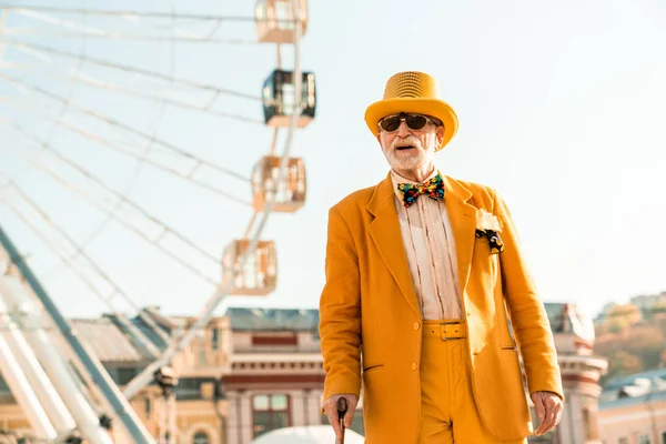 Old man in artistic suit and hat standing near ferris wheel — 스톡 사진