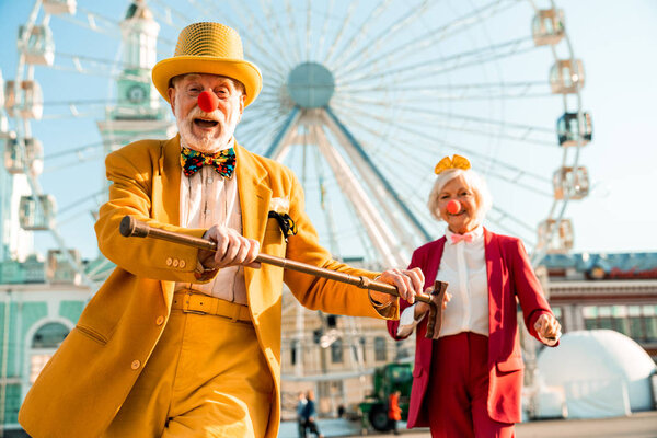 Happy senior couple in funny clothes having great time near ferris wheel